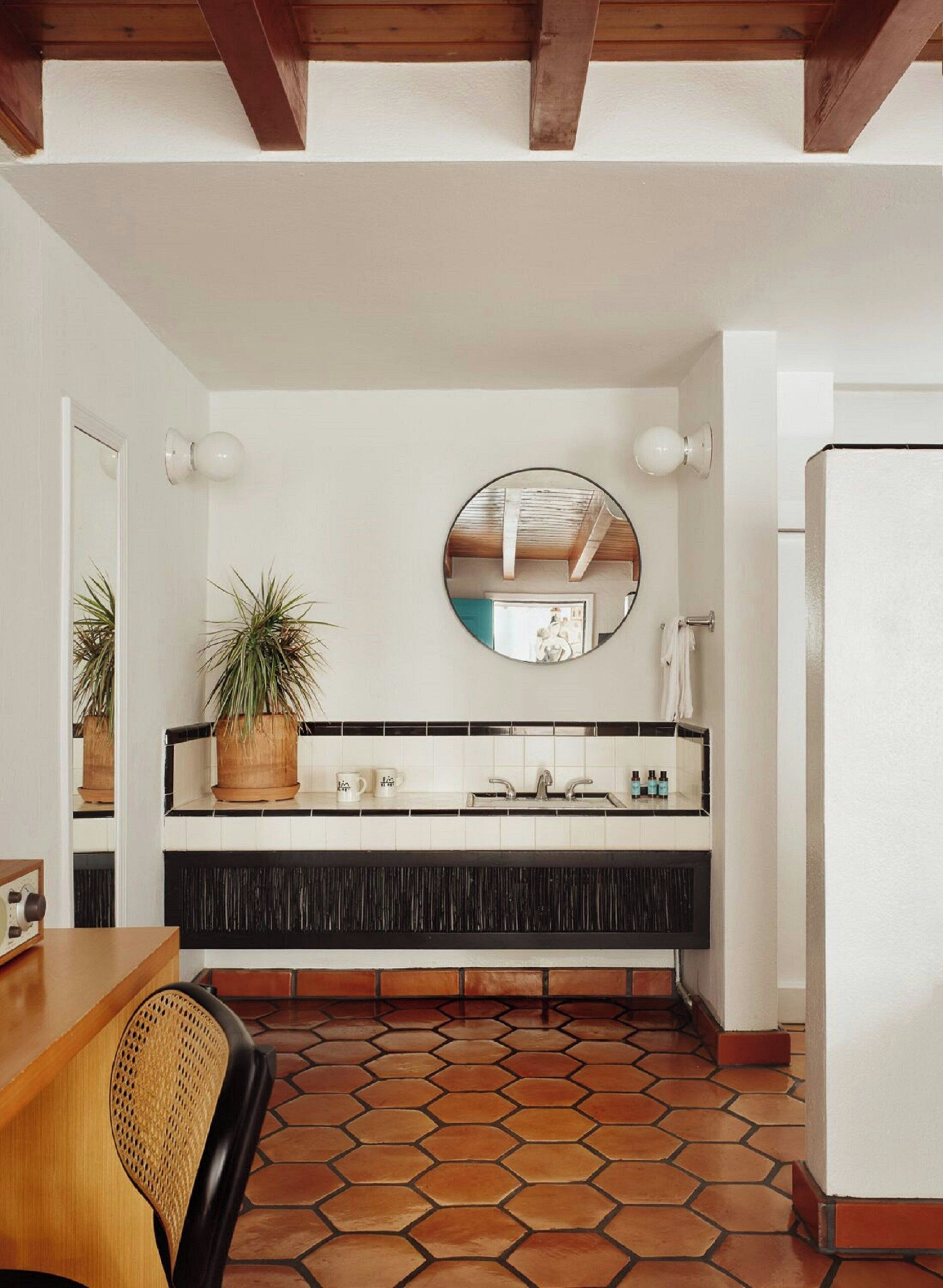 A bathroom with a round mirror, a sink, and a potted plant.
