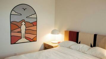Une chambre d’hôtel comprenant un lit, une table de chevet avec une lampe, une œuvre d’art murale et une tête de lit ornée d’un motif géométrique.