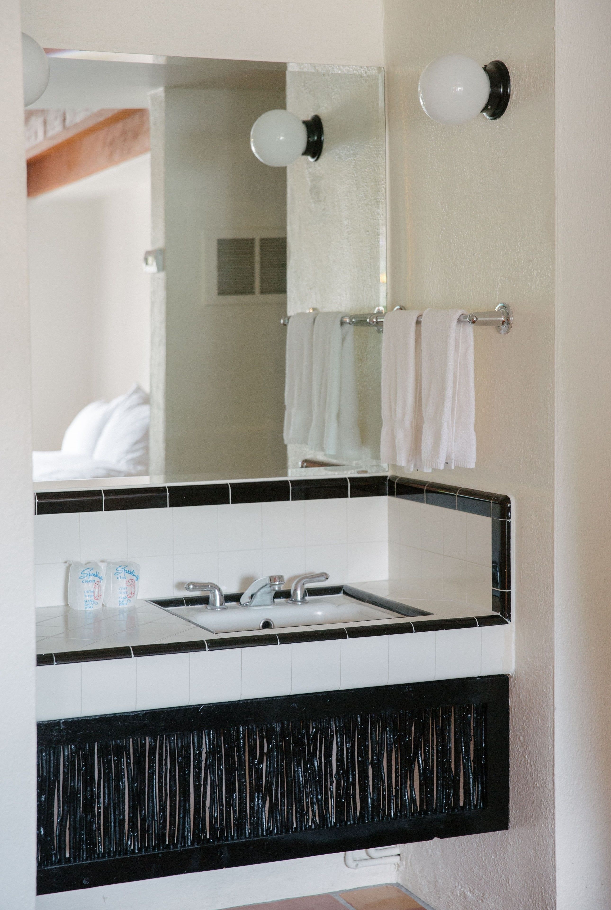 Un baño con un lavamanos de azulejos blanco y negro, un espejo y dos lámparas de pared.