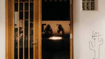 A room with a wooden door, a small table with a light source, and a wall with a simple line drawing.