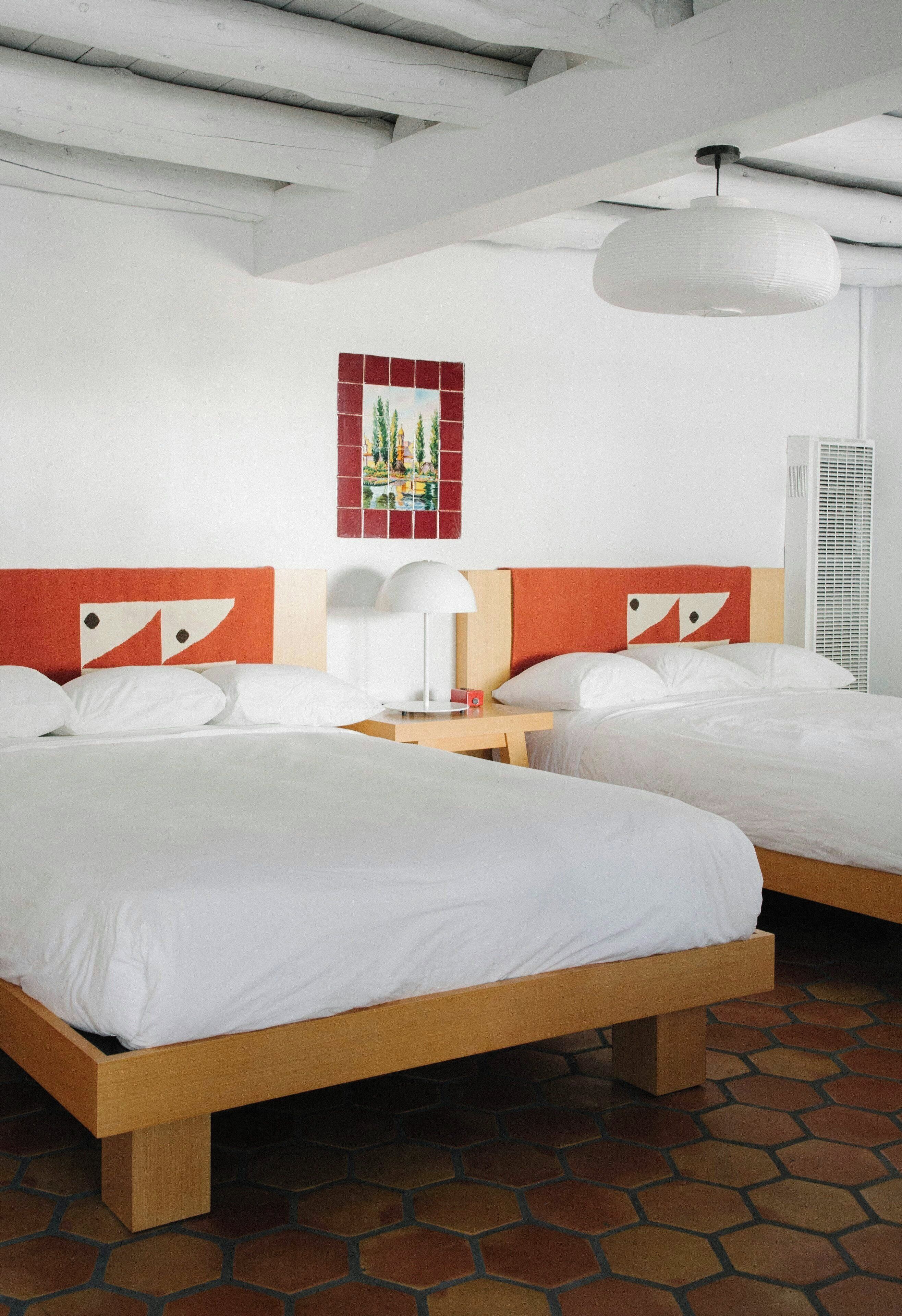 Een hotelkamer met twee bedden, een nachtkastje, een lamp en een kunstwerk aan de muur.