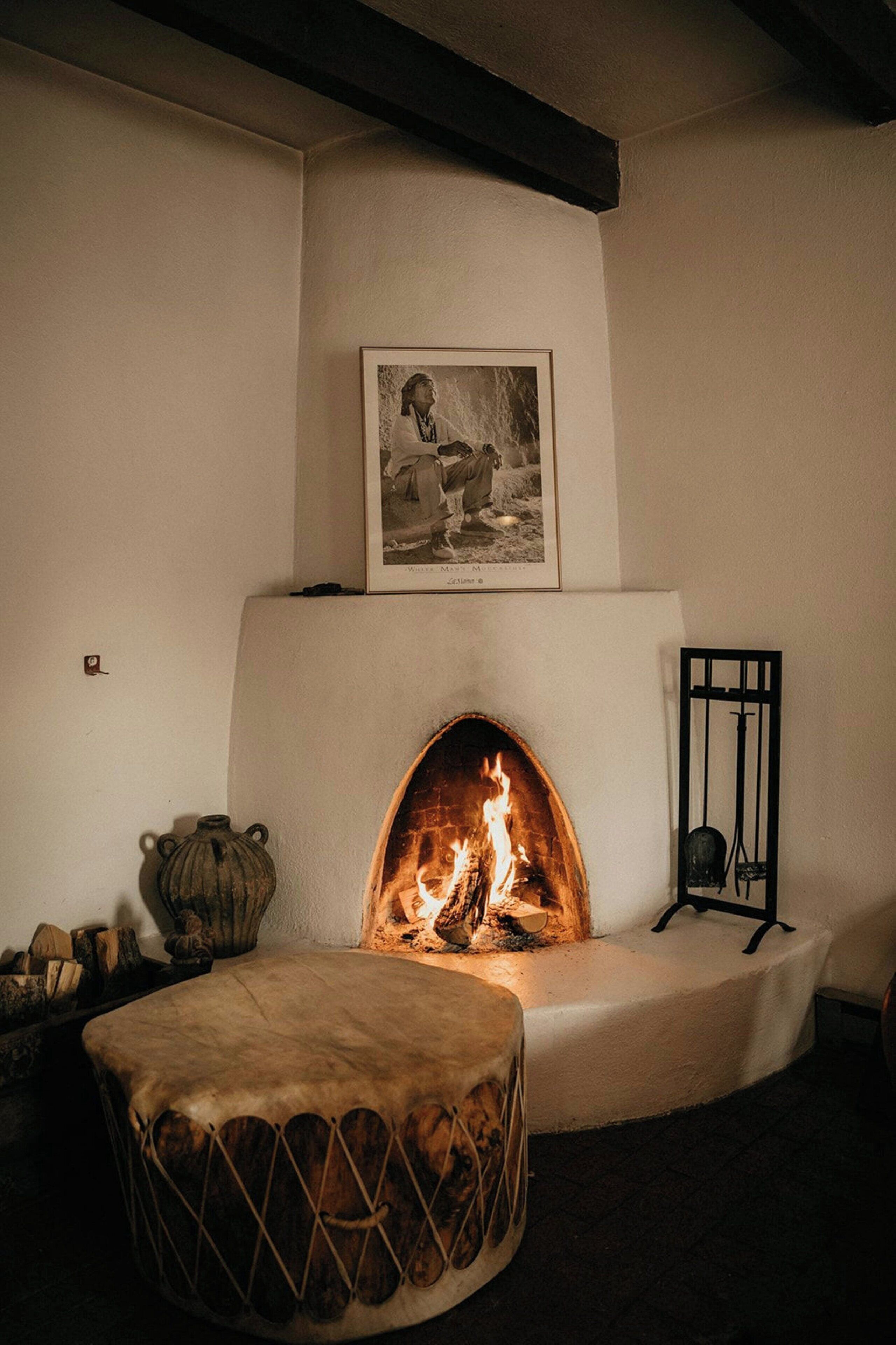 Ein Kamin mit Feuer, ein gerahmtes Bild darüber und ein kleiner Tisch davor.