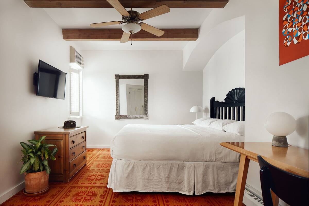 A bedroom with a bed, a dresser, a mirror, a ceiling fan, and a TV.