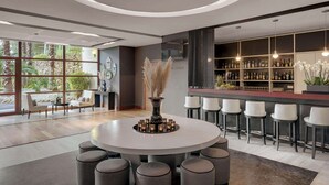 Un espace bar moderne avec une table ronde et des tabourets de bar, une grande fenêtre donnant sur un paysage verdoyant, et un comptoir bien garni de différentes bouteilles.