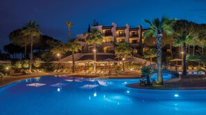A hotel with a pool, lounge chairs, and palm trees.
