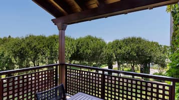 A wooden balcony with a table and chairs, surrounded by a lattice fence, overlooking a row of trees.