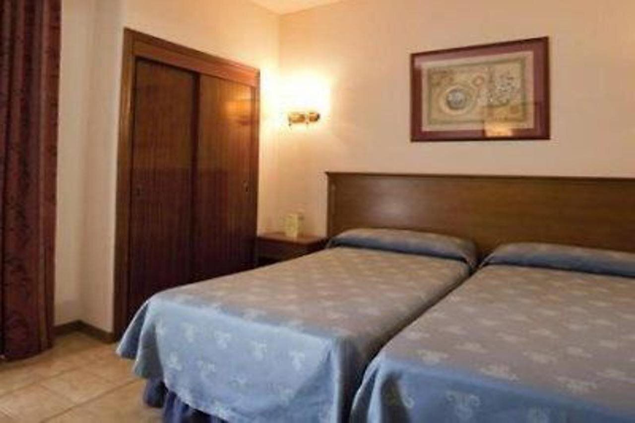 Habitación de hotel con dos camas, un armario de madera, una mesita de noche y un cuadro en la pared.