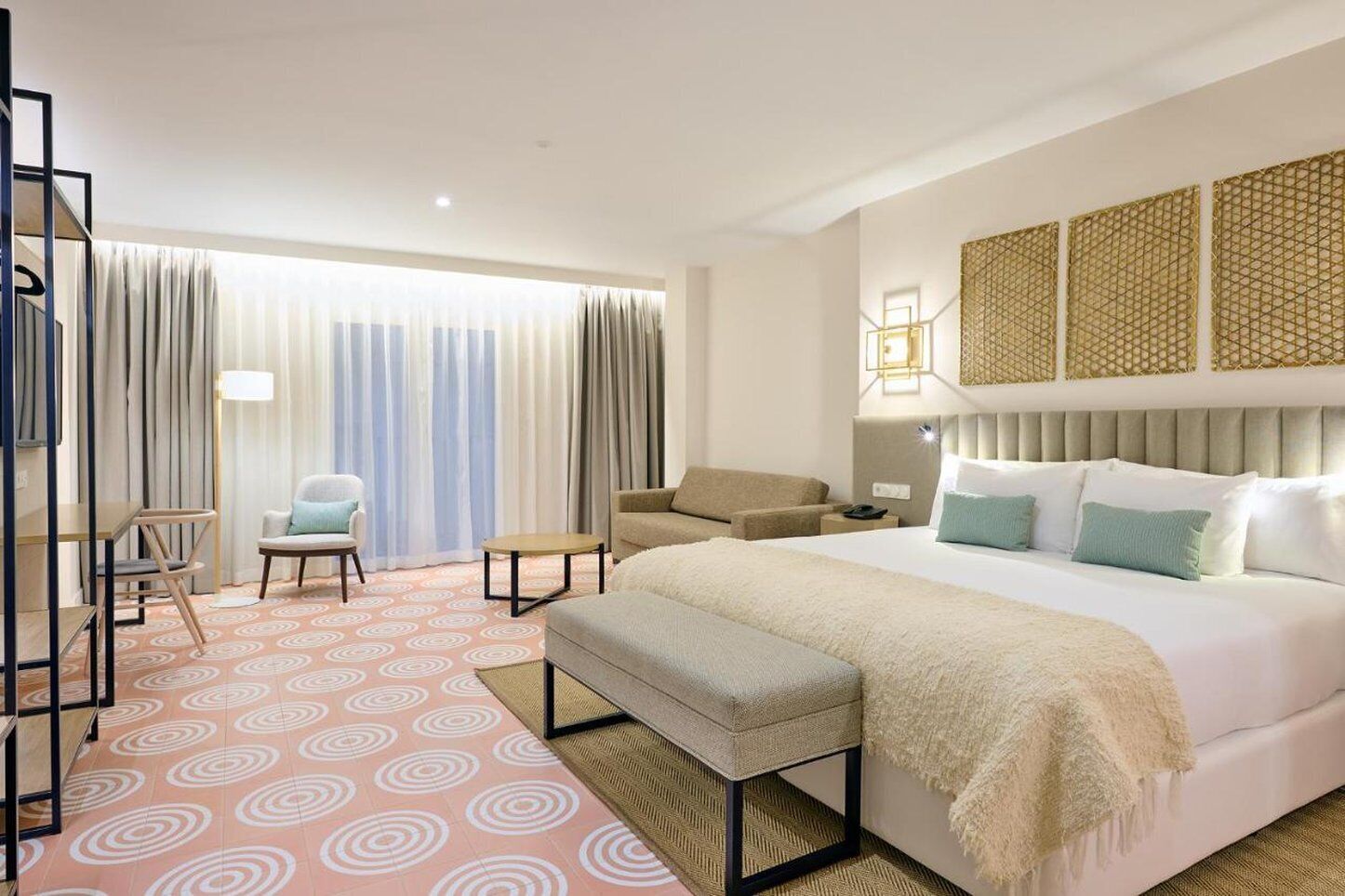 Una habitación de hotel con una cama grande, un sofá, una silla, una mesita y un televisor.