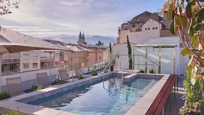 A rooftop pool with lounge chairs, a glass-enclosed area, and a view of buildings and mountains in the background. - Montecarlo (Granada)