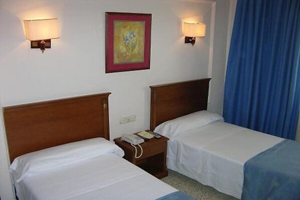 A hotel room with two single beds, a nightstand with a phone, and wall-mounted lamps. - Montecarlo (Granada)