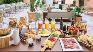 A breakfast buffet with various food items and drinks, a seating area with tables and chairs, and a view of the building's exterior. - Montecarlo (Granada)