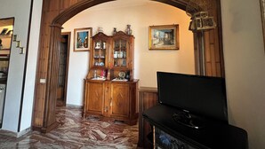 Un soggiorno con un arco in legno, una televisione, un mobile con vetrate e due quadri appesi al muro.