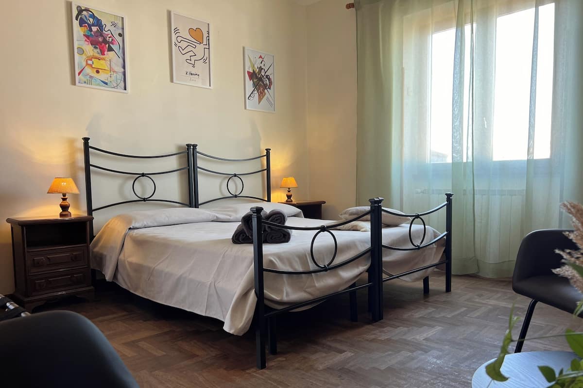 Una camera da letto con un letto matrimoniale, due comodini con lampade, una sedia e opere d'arte alle pareti.