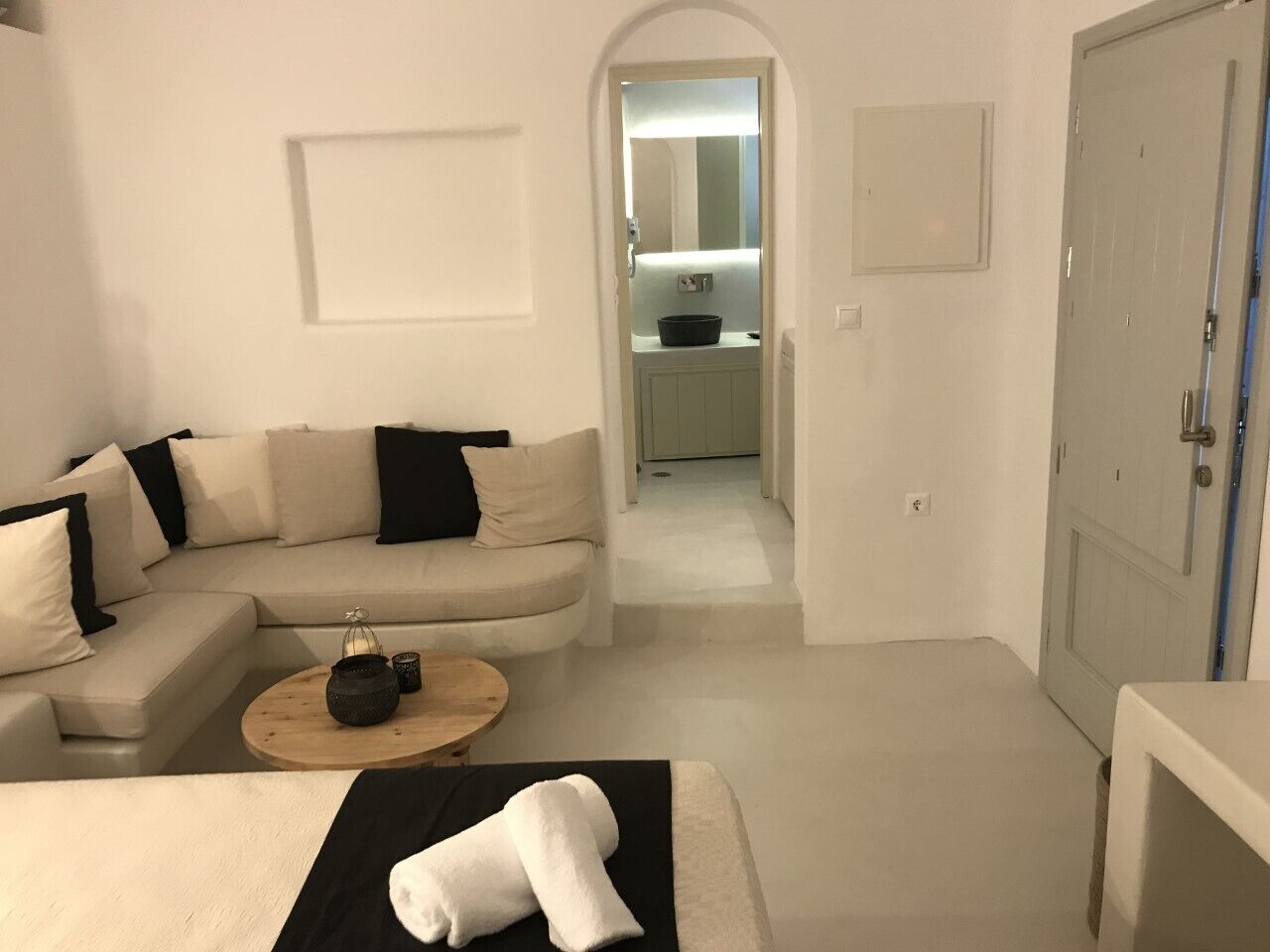 Een moderne, minimalistisch ingerichte kamer met een bank, een ronde houten tafel en een bed met een zwart-wit plaid.