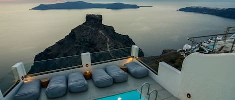 Zona junto a la piscina con vistas al mar y a las islas, un área de descanso con cojines y una pequeña mesa.