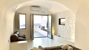 A modern hotel room with a large bed, a seating area with a view, and a stone wall. - Hotel Sunny Villas (Santorini)