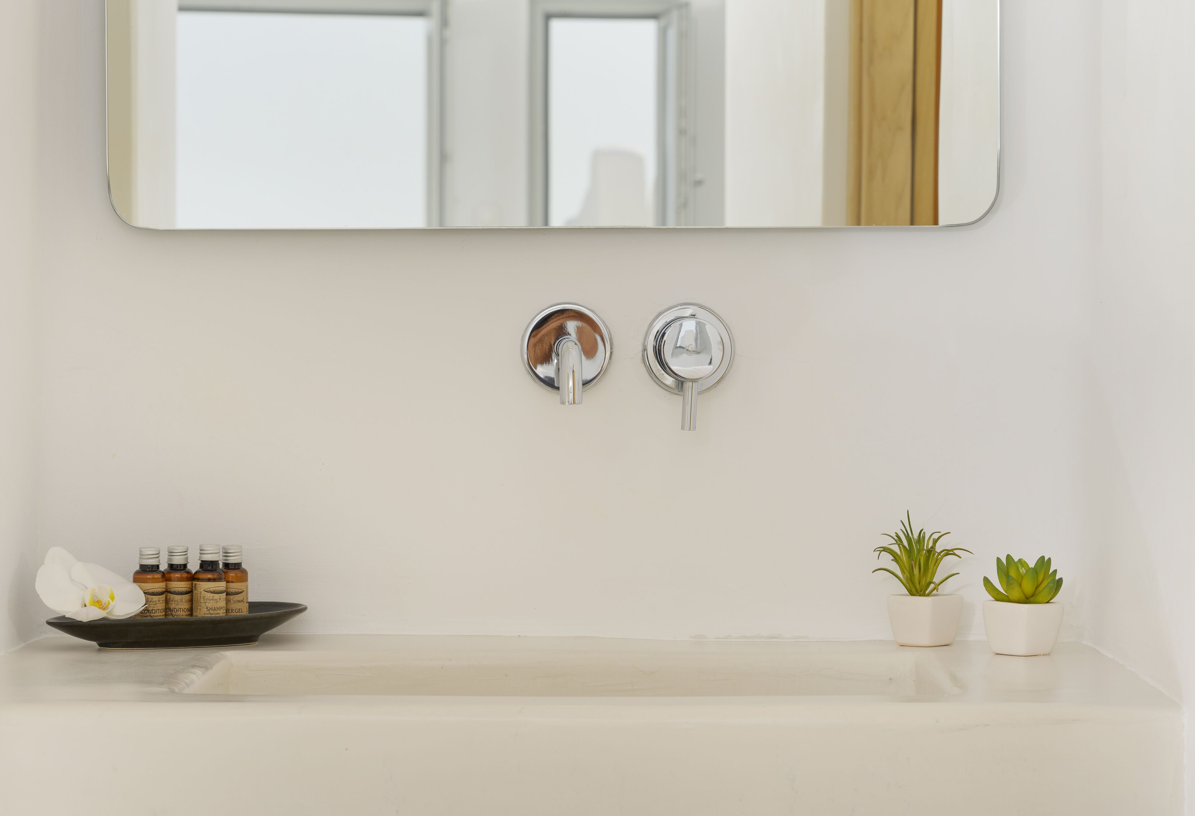 A bathroom with a white sink, two faucets, a mirror, and two potted plants.