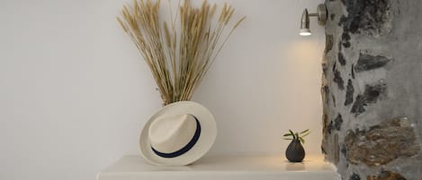 A white shelf with a vase of dried wheat stalks, a hat, and a small potted plant.