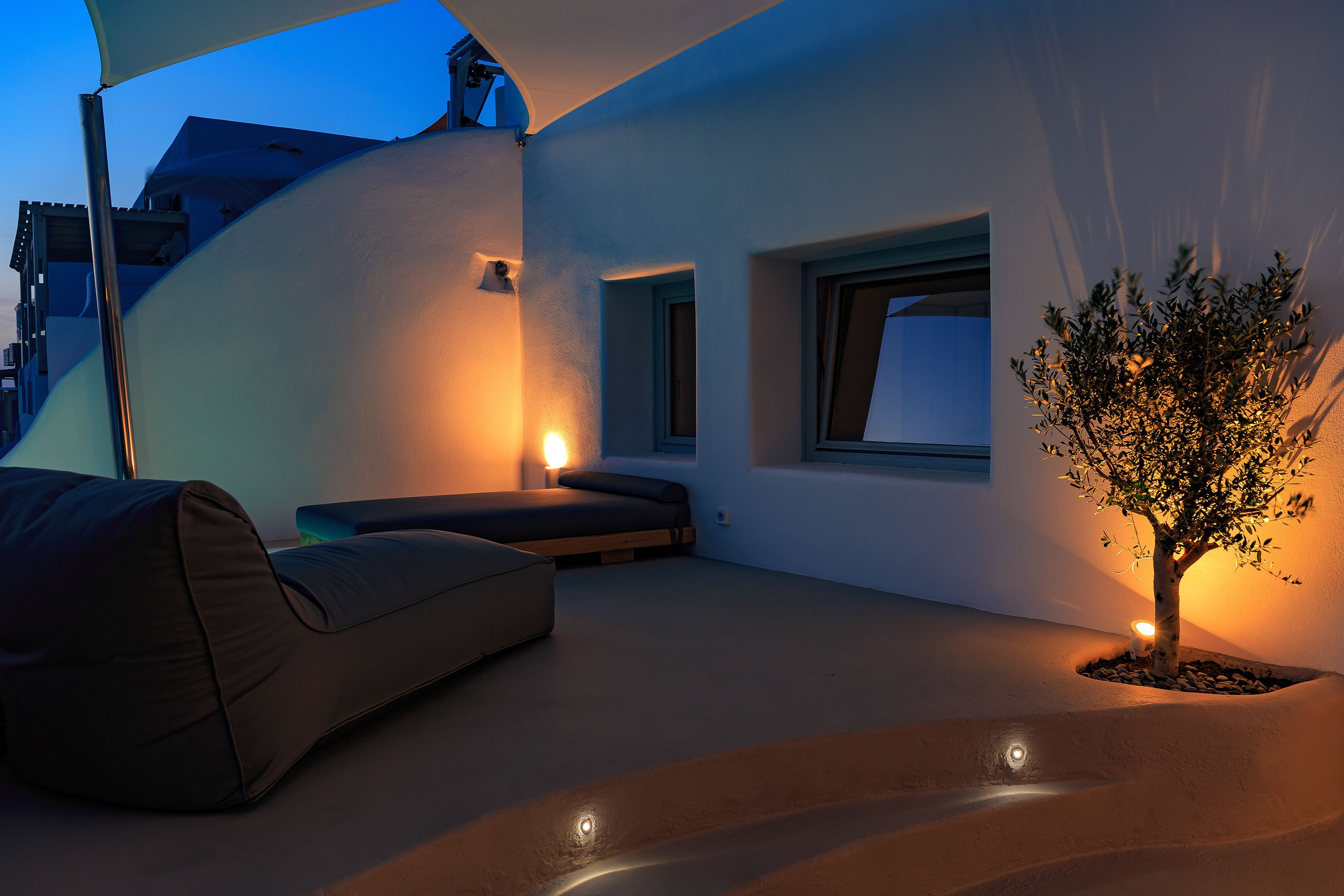 Un espacio exterior moderno con una banca curva, un árbol pequeño y una ventana.