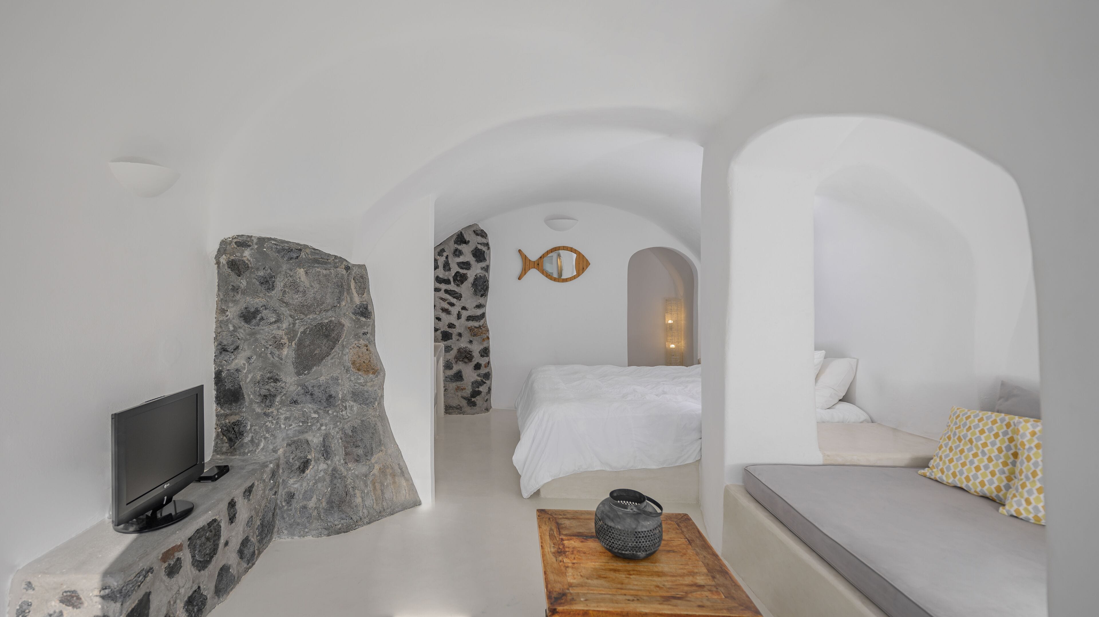 A minimalist room with a stone wall, a bed with white bedding, a wooden coffee table, and a sofa with patterned cushions.