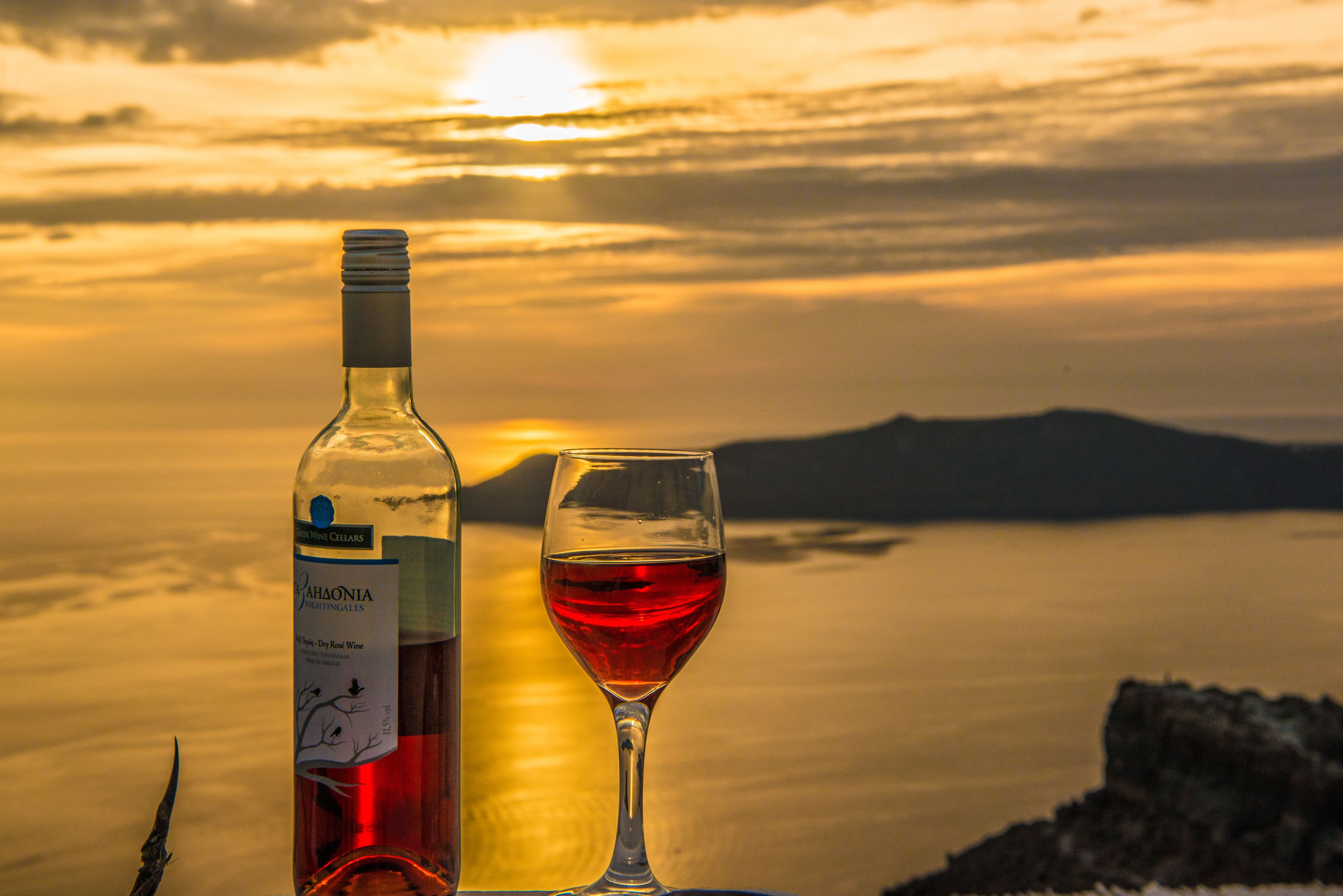 Une bouteille de vin et un verre de vin rouge sur une table, avec une vue sur le coucher de soleil.