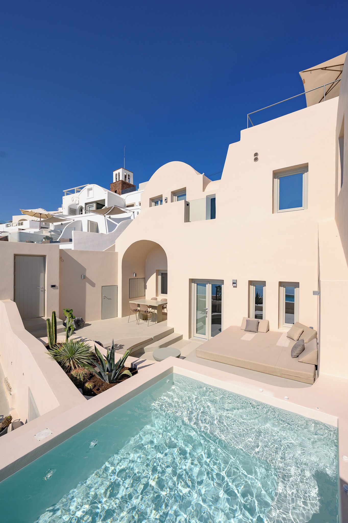 Un resort moderno con piscina, mobiliario exterior y un cielo azul despejado.