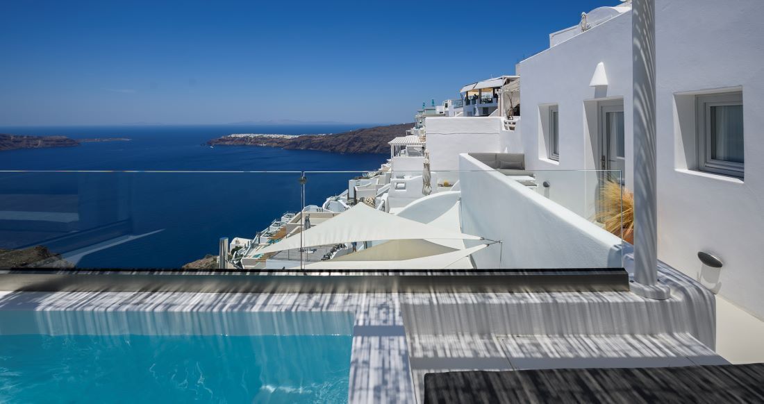 A modern white building with a pool overlooking a clear blue sea and distant land.