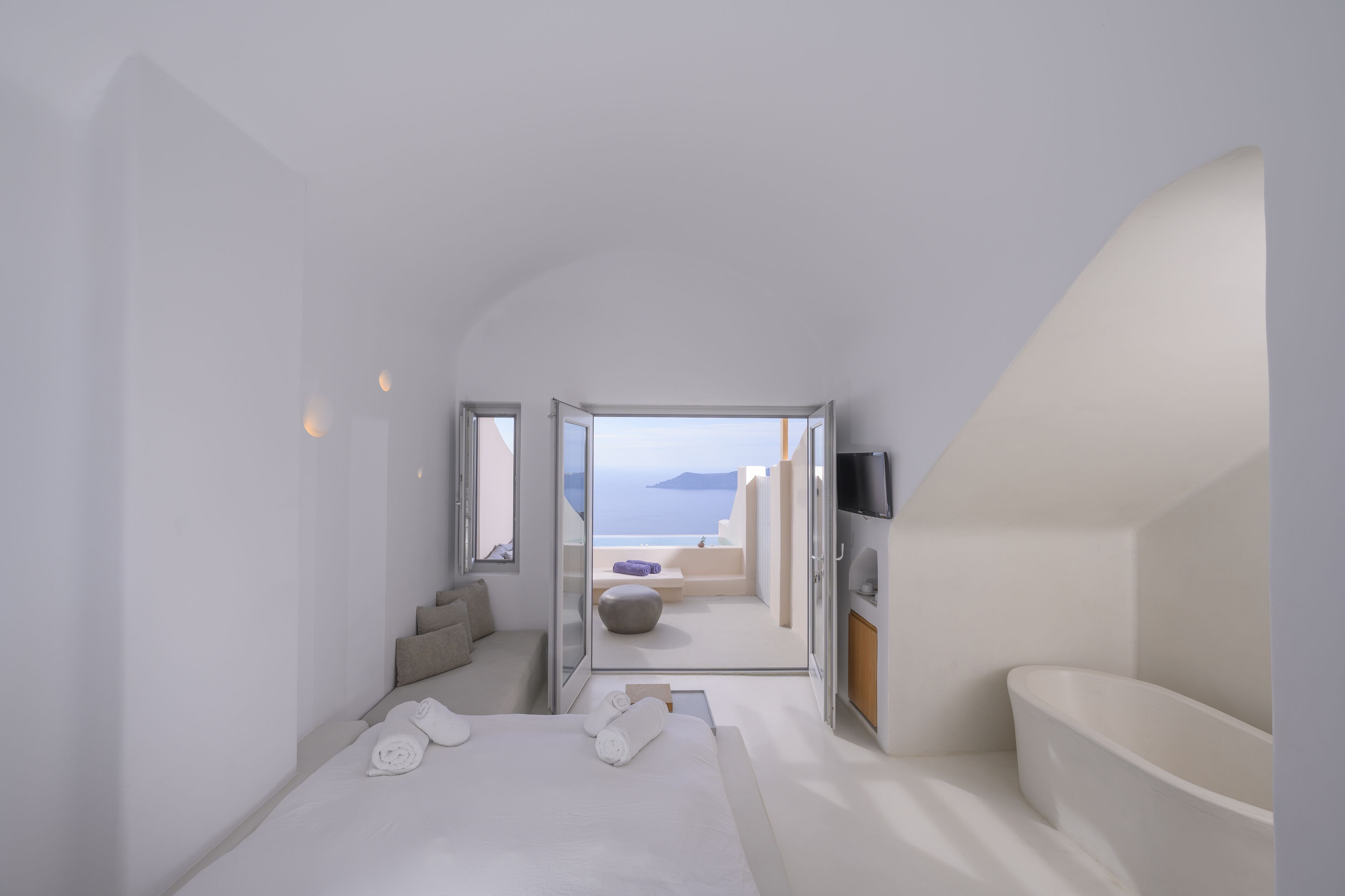 A modern bedroom with a bed, a bathroom, and a view of the sea.