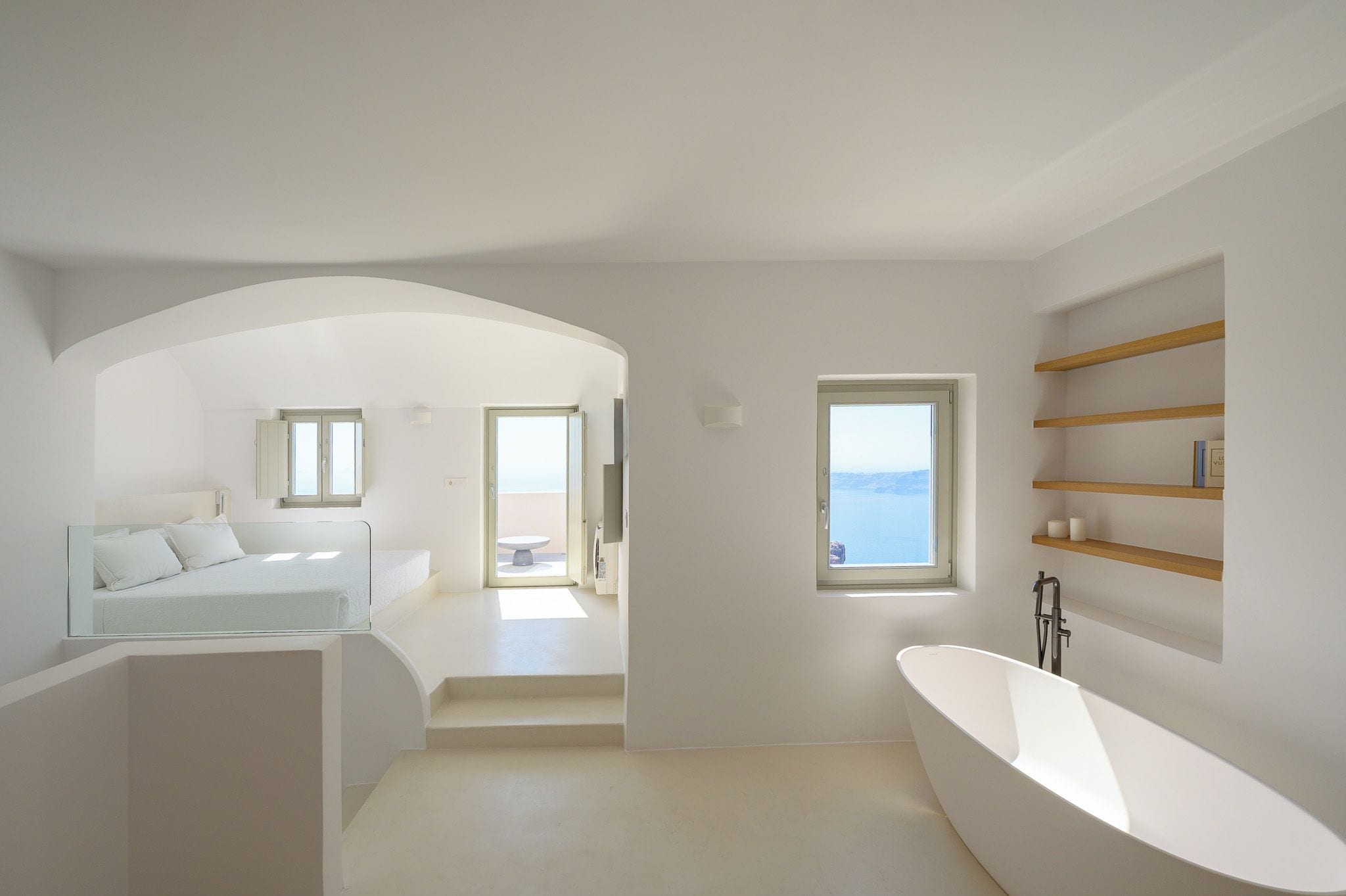 A modern bathroom with a freestanding bathtub, a glass-enclosed shower area, and a view of the sea through a window.