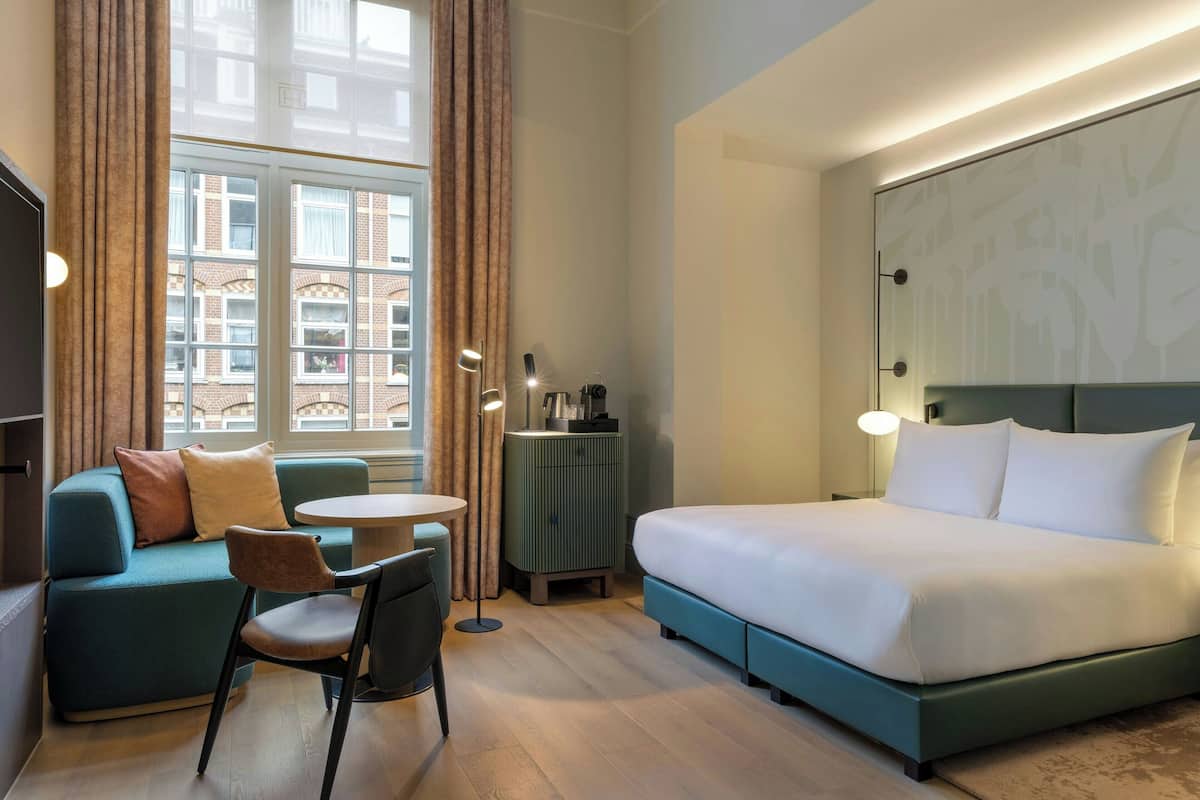 A hotel room with a bed, a sofa, a chair, a small table, and a nightstand.