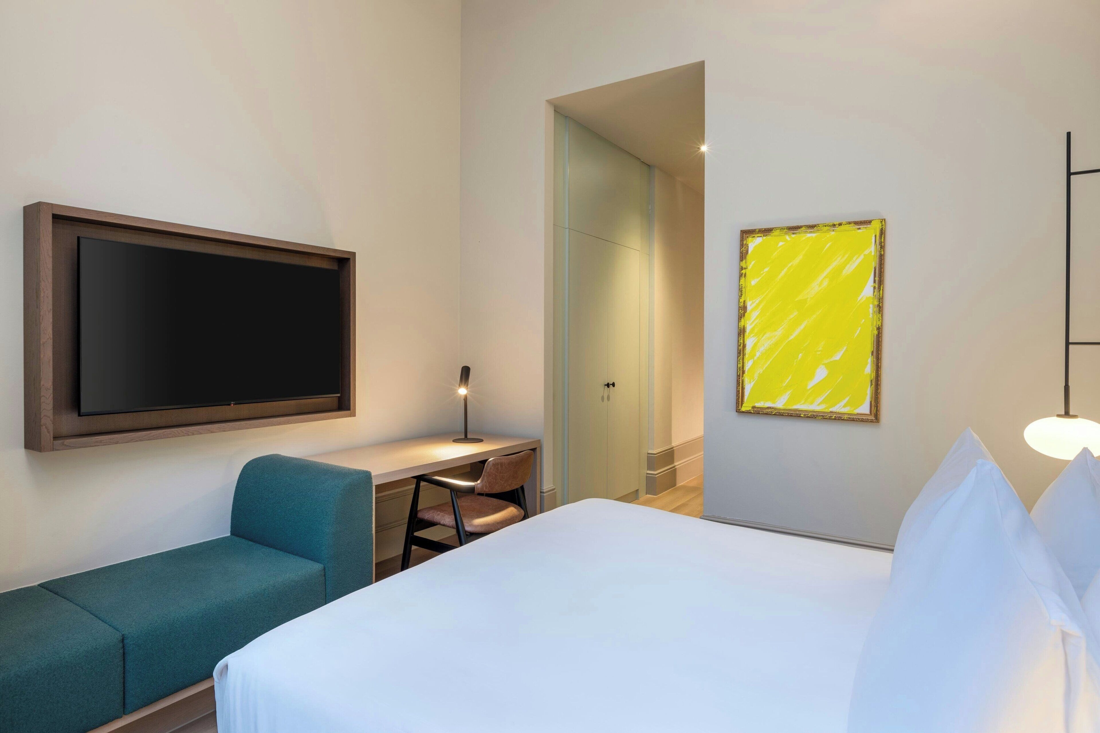 Habitación de hotel con cama, escritorio, silla, televisor y puerta que da a otra habitación.