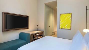 Habitación de hotel con cama, escritorio, silla, televisor y puerta que da a otra habitación.