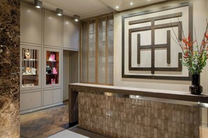 A reception area with a marble wall, a reception desk, and a potted plant. - The College Hotel Amsterdam, Autograph Collection (Amsterdam)