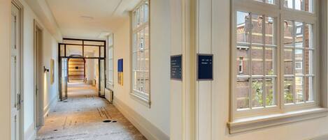A corridor with a polished floor, directional signs, and large windows with a view of a brick building.