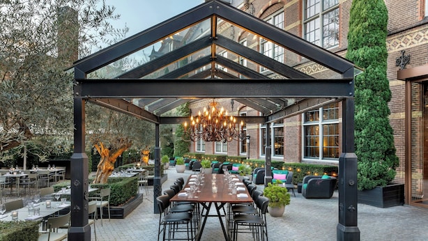 A covered outdoor dining area with a long table, chairs, and a chandelier. - The College Hotel Amsterdam, Autograph Collection (Amsterdam)