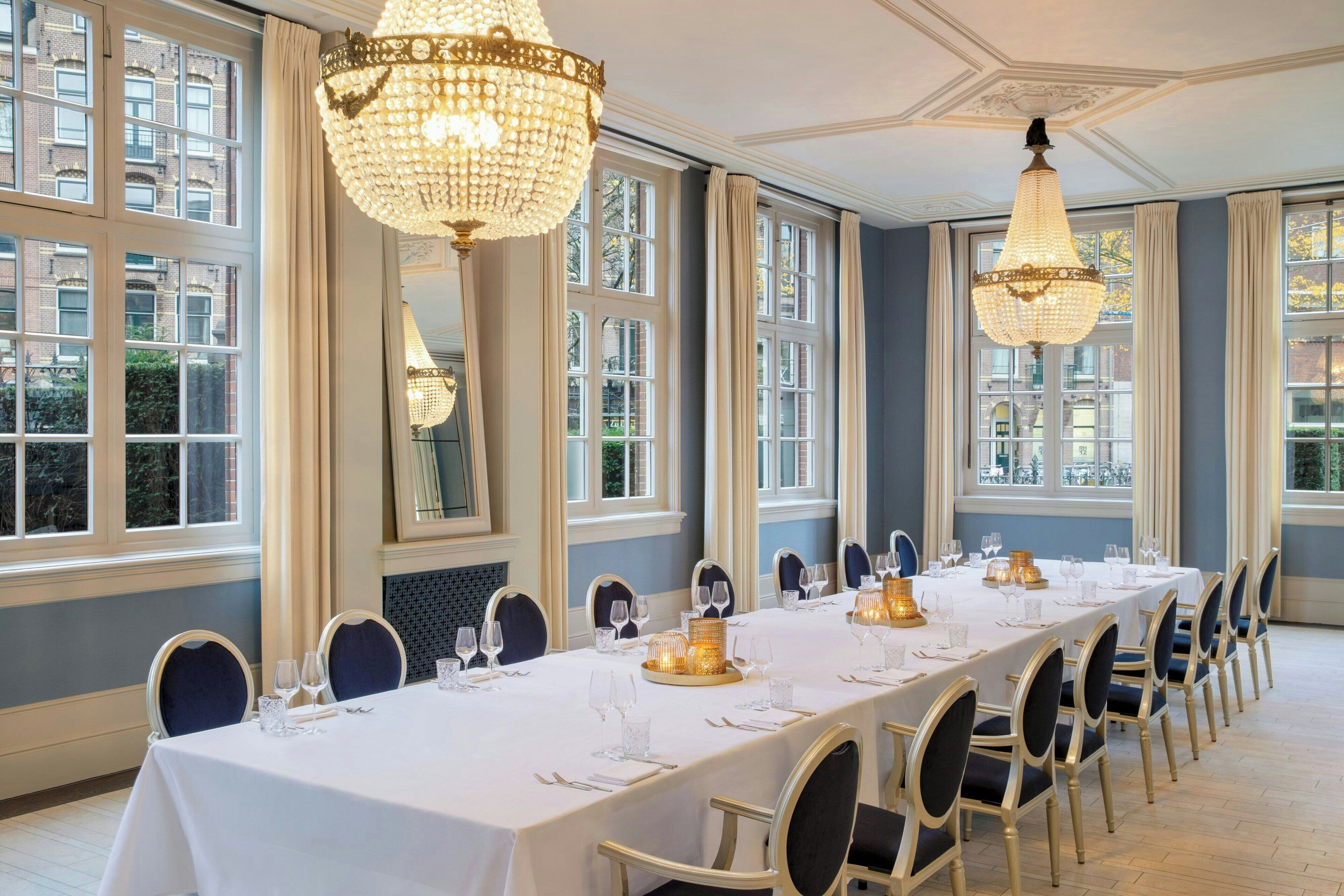 Una larga mesa de comedor dispuesta para un evento formal con candelabros, sillas y vistas al exterior.
