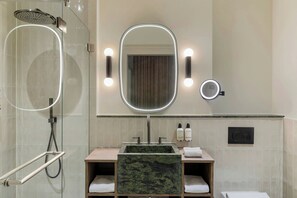 A bathroom with a glass-enclosed shower, a vanity with a green marble sink, and two wall-mounted mirrors with lights. - The College Hotel Amsterdam, Autograph Collection (Amsterdam)