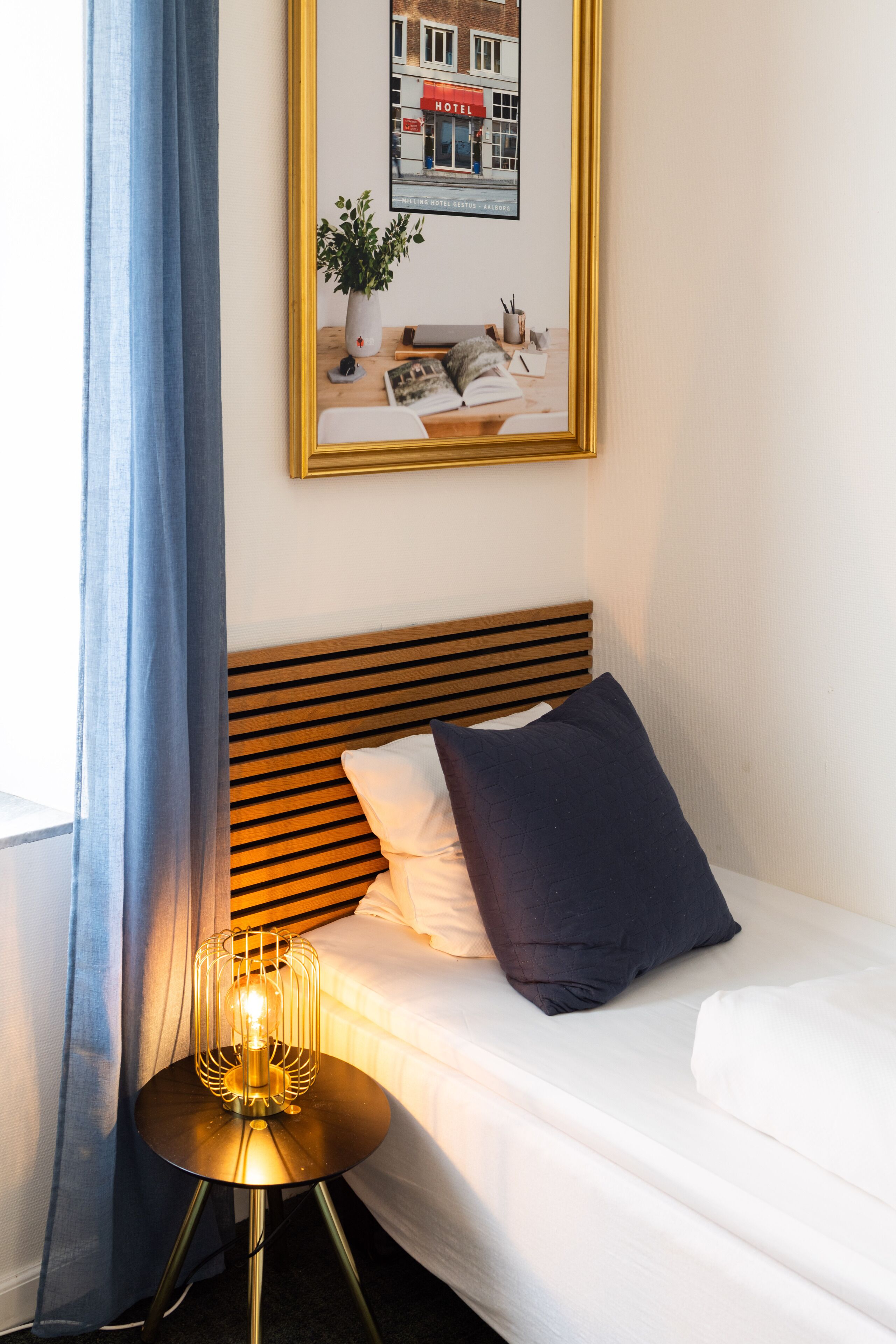 Un lit bien fait, avec une tête de lit en bois, une lampe de chevet et un tableau encadré au-dessus.