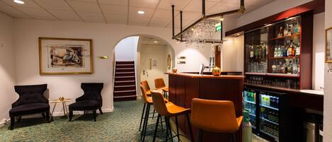 A bar area with stools, a refrigerator stocked with beverages, and a patterned carpet.