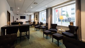 A hotel room with a dining area, multiple chairs, a table, a television, and large windows with curtains. - Milling Hotel Ansgar (Odense)