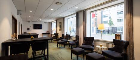 A hotel room with a dining area, multiple chairs, a table, a television, and large windows with curtains.
