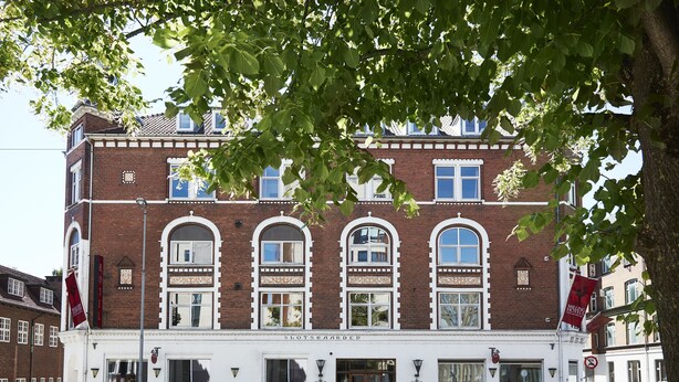 A traditional brick building with arched windows and a white facade, featuring a sign that reads "SLOTSGAARDEN." - Milling Hotel Ansgar (Odense)