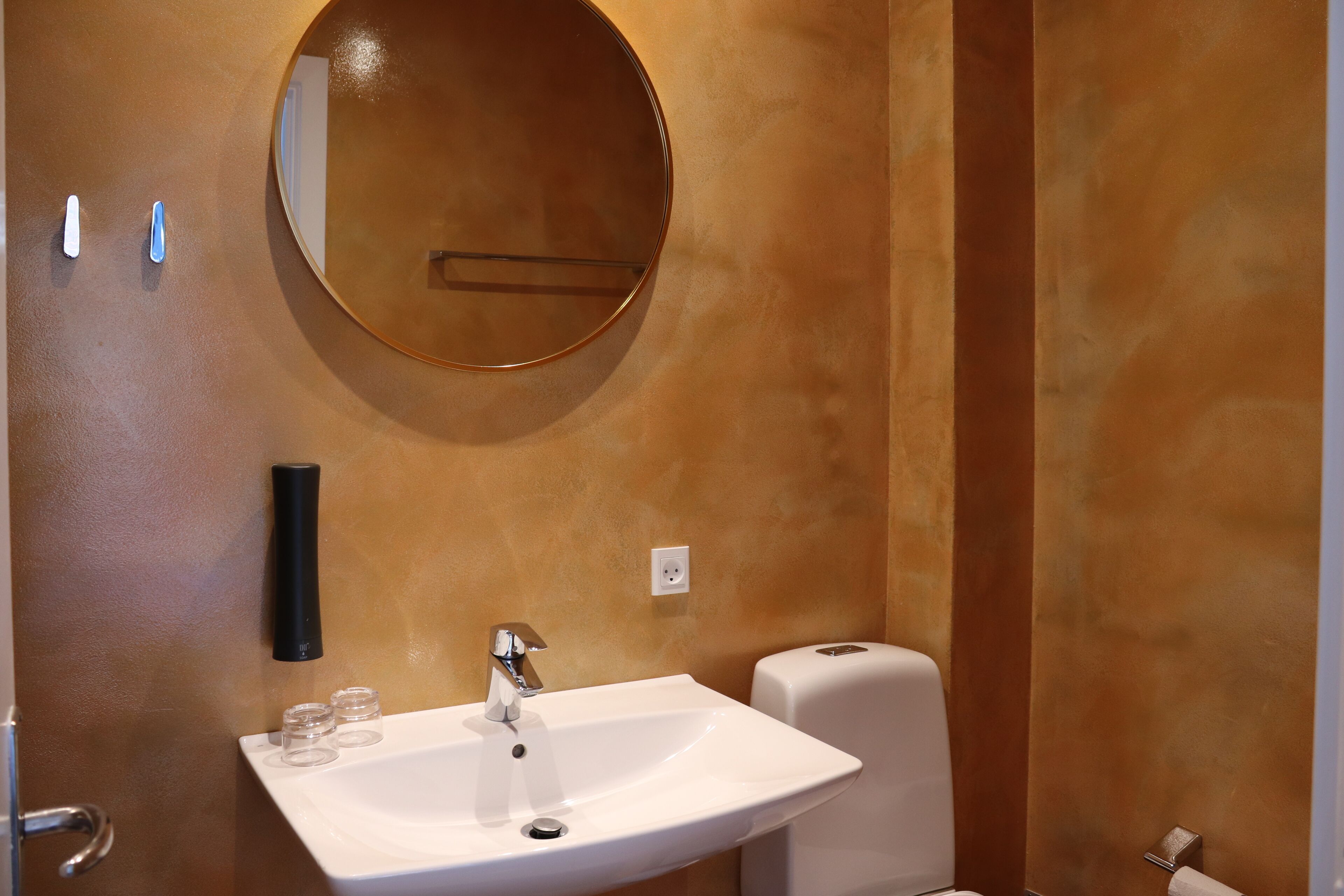 A bathroom with a white sink, a round mirror, and a toilet.