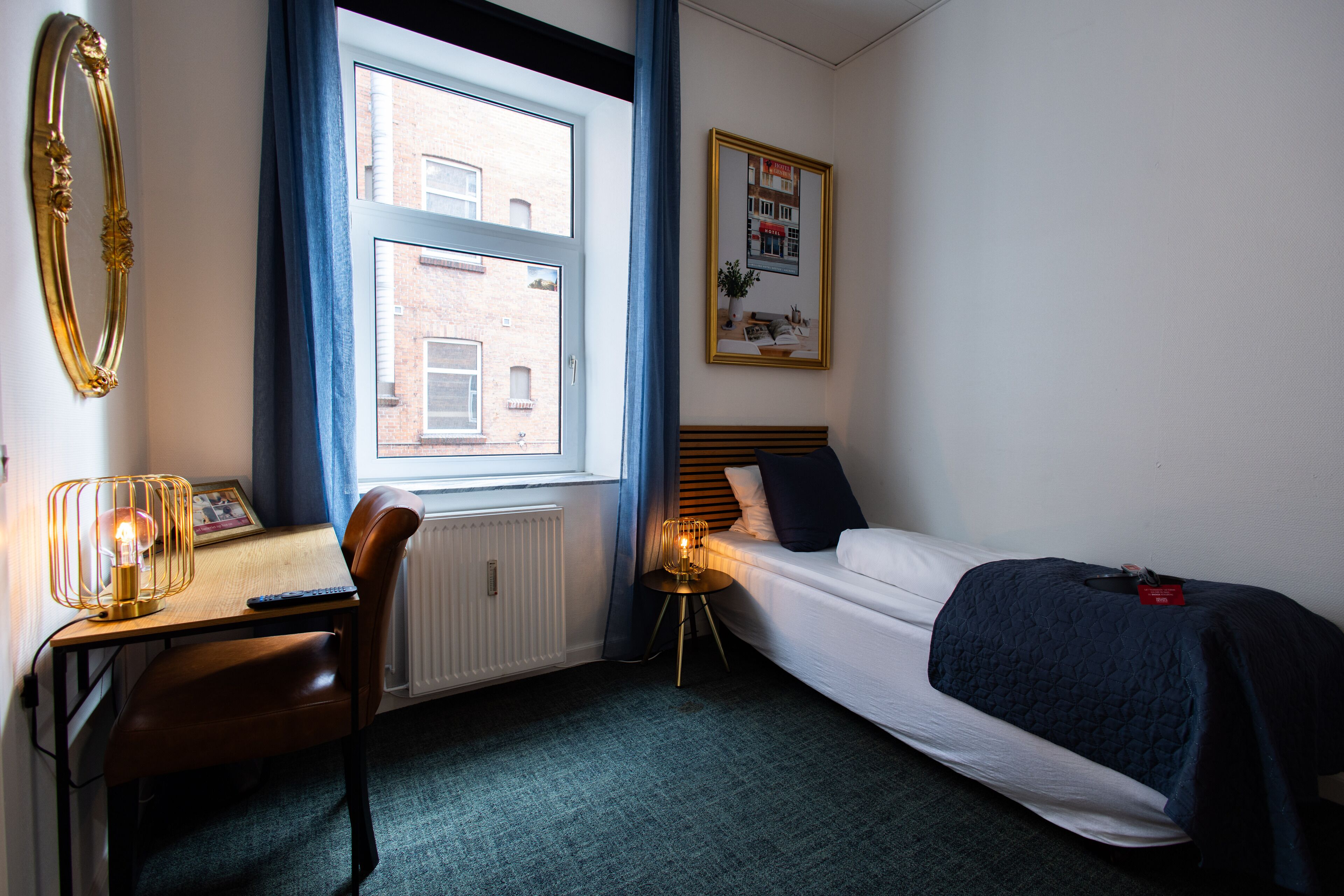 A small, well-lit room with a desk, chair, and a single bed.