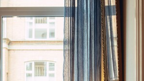 A hotel room with a wooden desk, a lamp, a framed picture, and a view of buildings through a window with curtains. - Milling Hotel Ansgar (Odense)