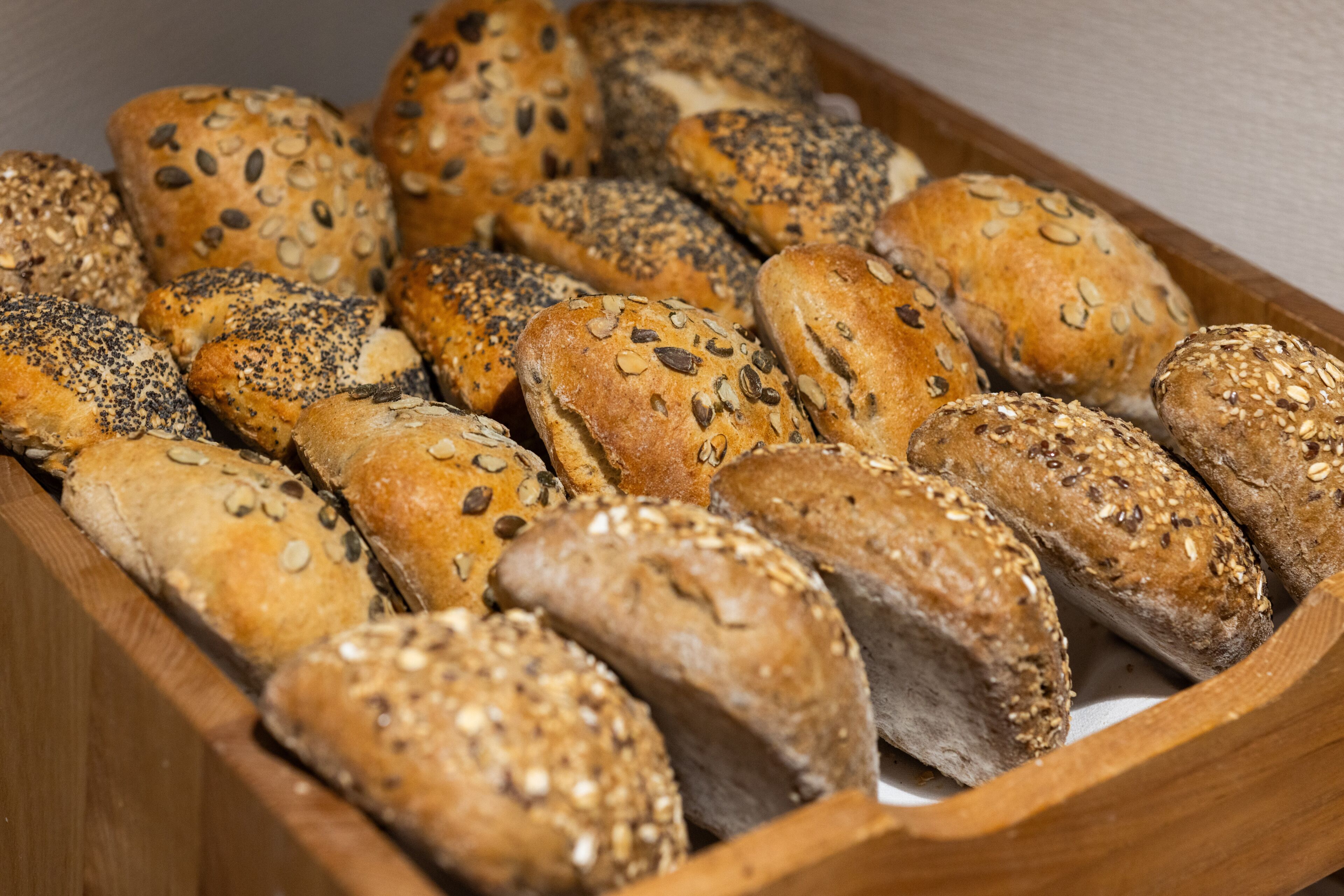 A wooden tray filled with various types of seeded bread.