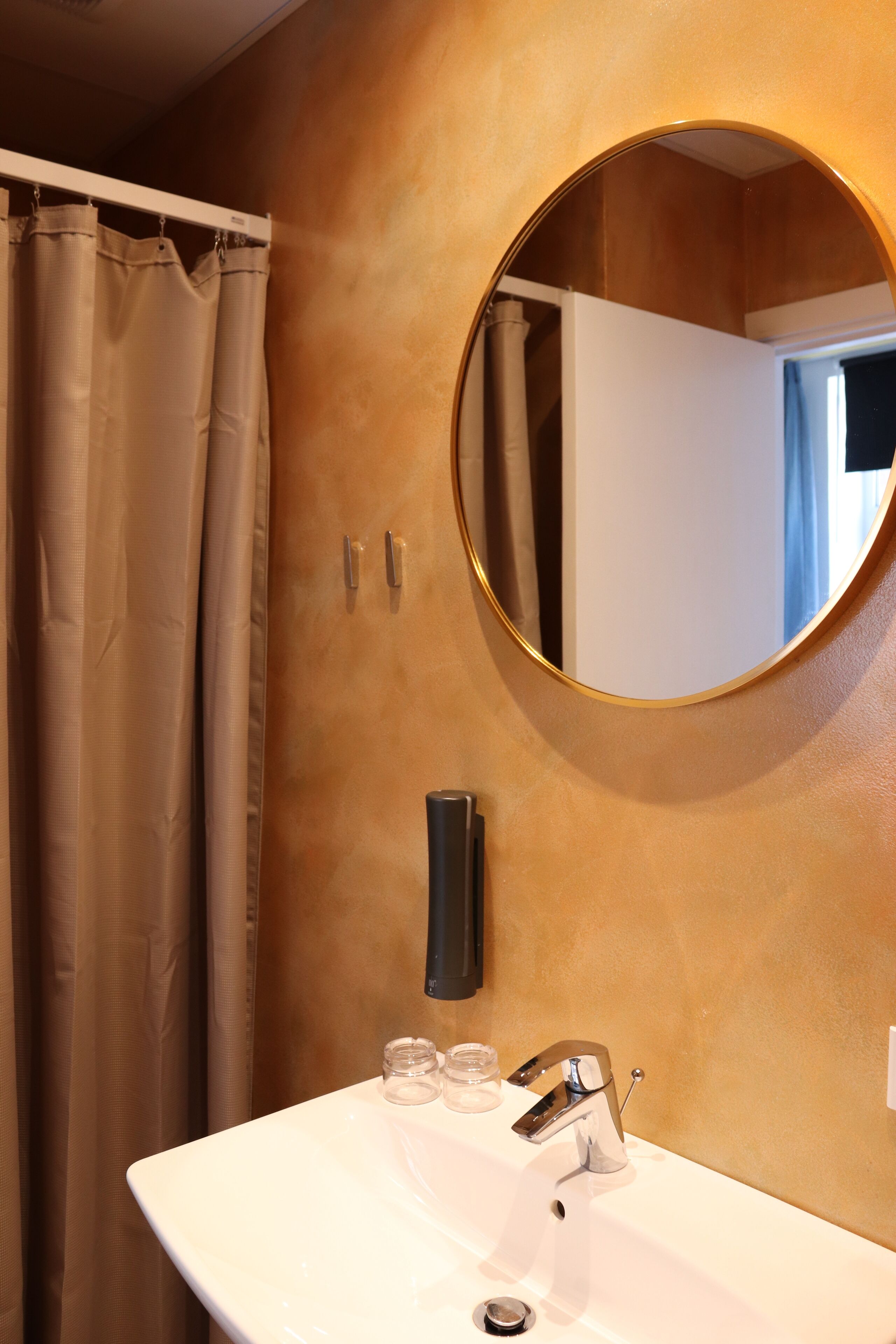 A bathroom with a white sink, a round mirror, and a beige curtain.