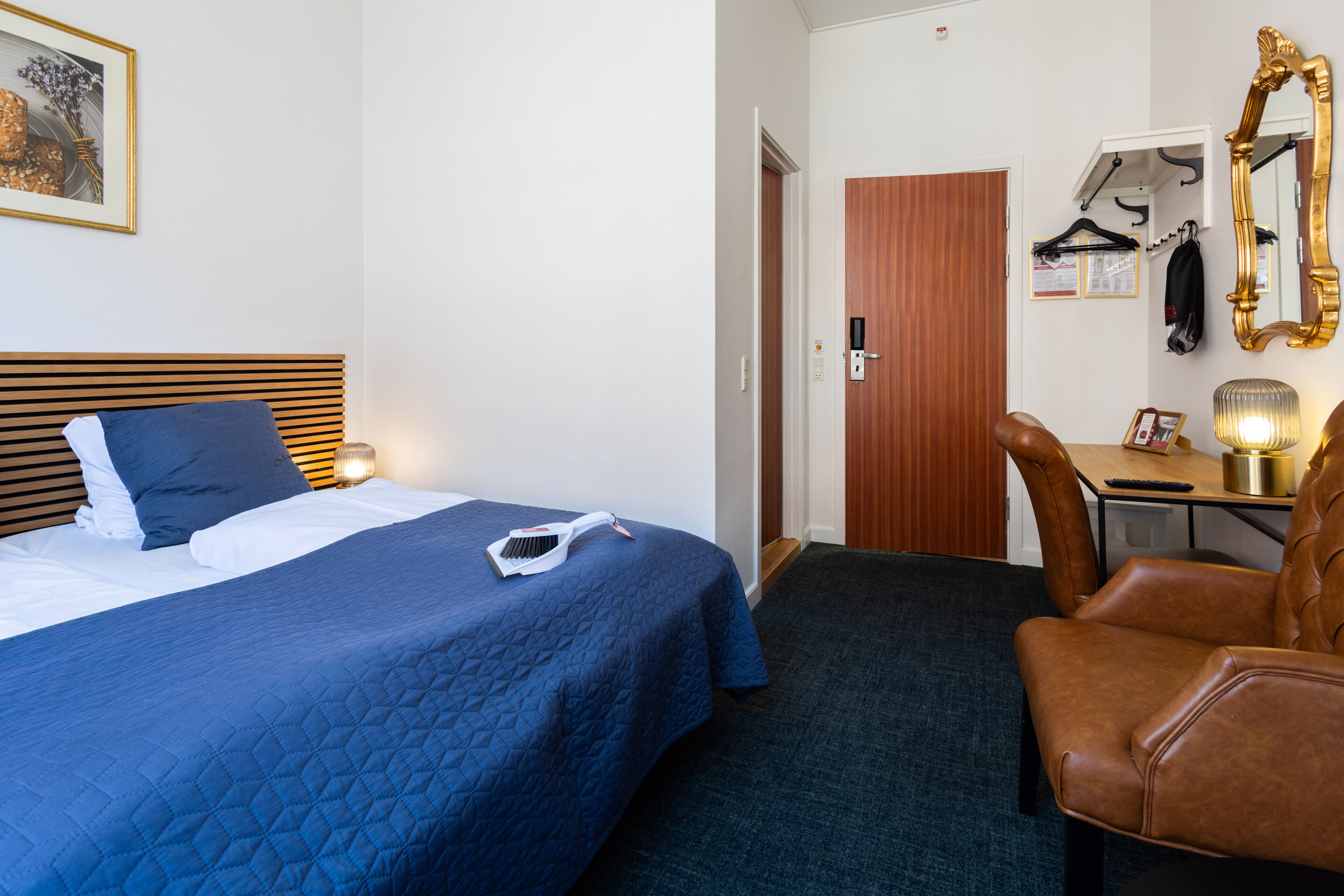 A hotel room with a bed, a desk, a chair, a mirror, and a door.