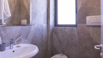 A bathroom with a large mirror, a sink, a bidet, and a window.