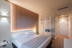 Une chambre d’hôtel moderne équipée d’un lit, d’une table de chevet et d’une armoire avec un miroir.